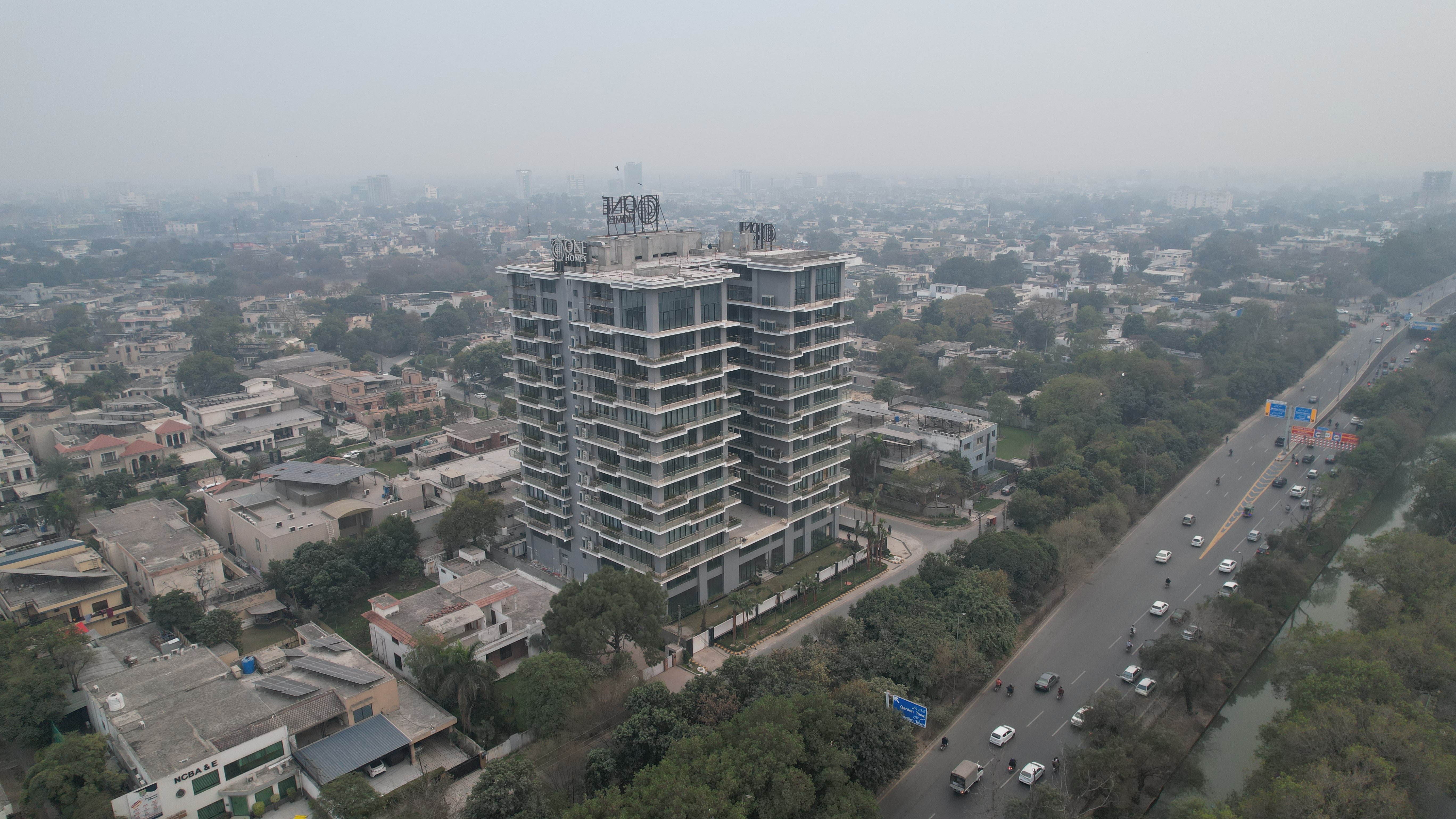 One Canal Road stands tall amidst trees on the inside of a main road, surrounded by other smaller buildings