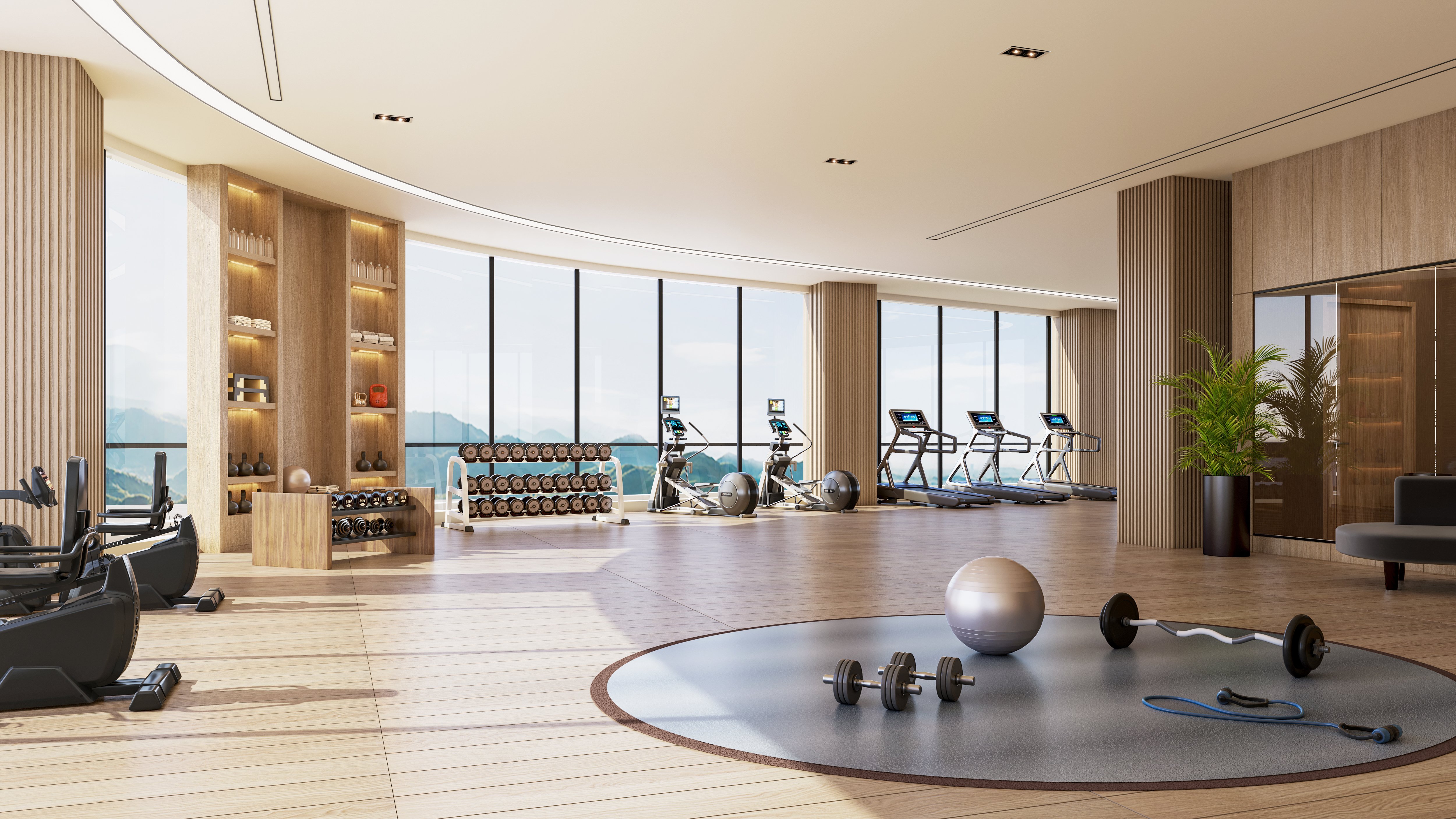 A large, spacious gym with windows lining the curved side overlooking mountains, with modern equipment facing the outside