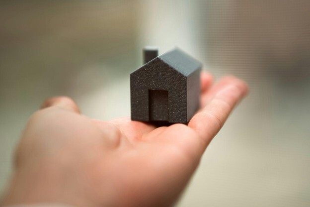 A blurred hand holding a 3-D figure of a house in charcoal grey
