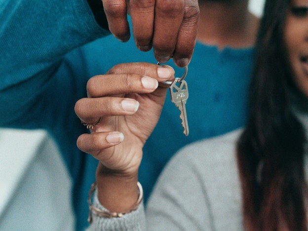 A zoomed-in image shows a person in blue handing a single house key over to a woman in front