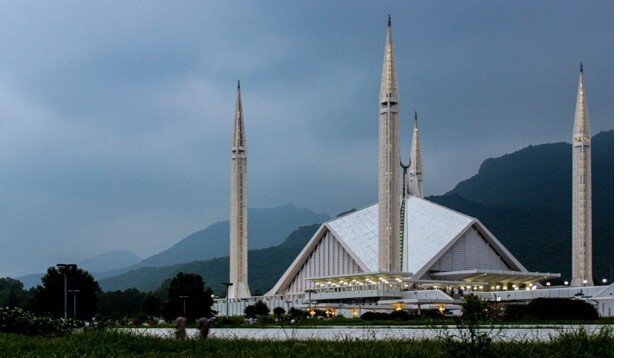Faisal Mosque in Islamabad against a silhouette of mountains and surrounded by greenery