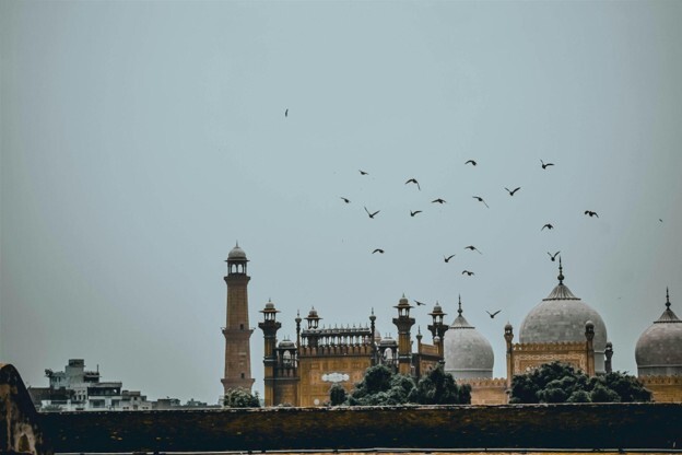 Scenic view of Badshahi Mosque and Lahore Fort with birds flying in the sky above, capturing the cultural heritage and timeless appeal of Lahore.