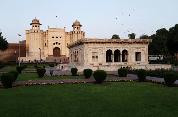 Lahore fort and gardens against a light blue sky dotted with flying birds
