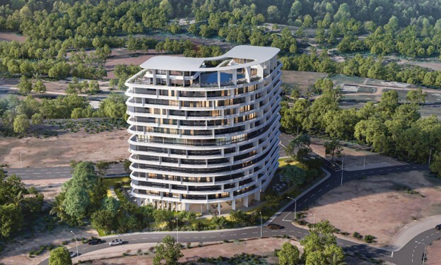 : A curved building stands tall amidst plots of empty land, trees, and roads