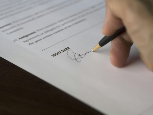 A close-up of a hand holding a black and gold pen while signing an official contract, symbolising secure and transparent property agreements aligned with British standards.