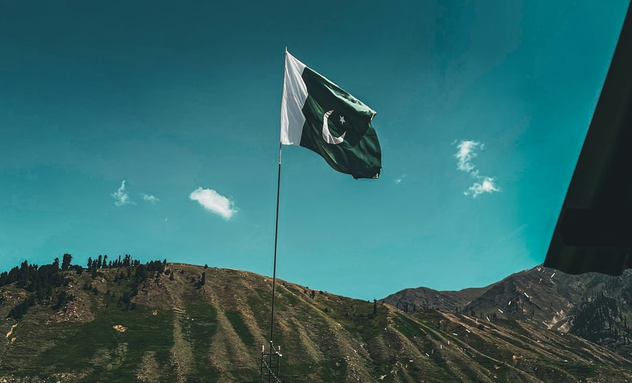 A Pakistani flag mounted on the side of rocky terrain with a bright blue sky in the background