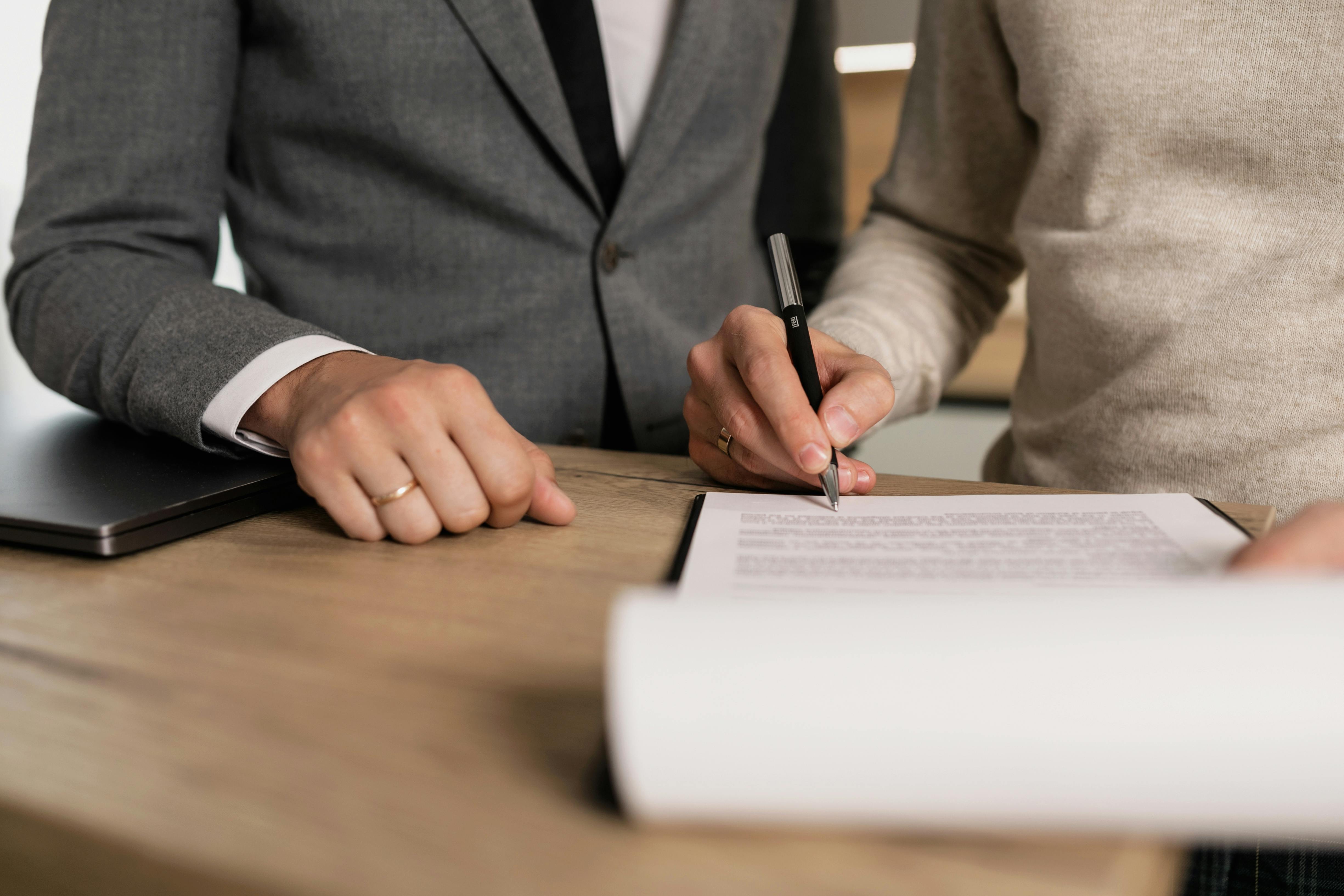 Two people sit together as one holds a pen above a document