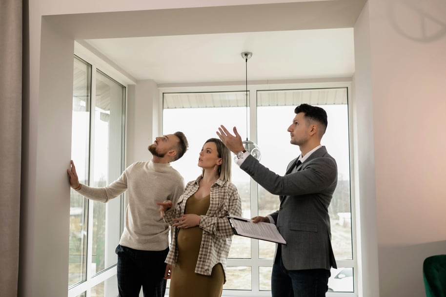 A man shows a couple an apartment as they stand by a window, examining it