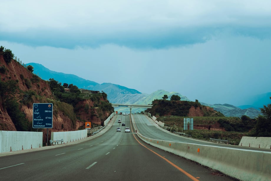 A stretch of motorway in Pakistan with mountains in the distance and a sign to the left showing distances to Gilgit, Naushera, and Abbottabad