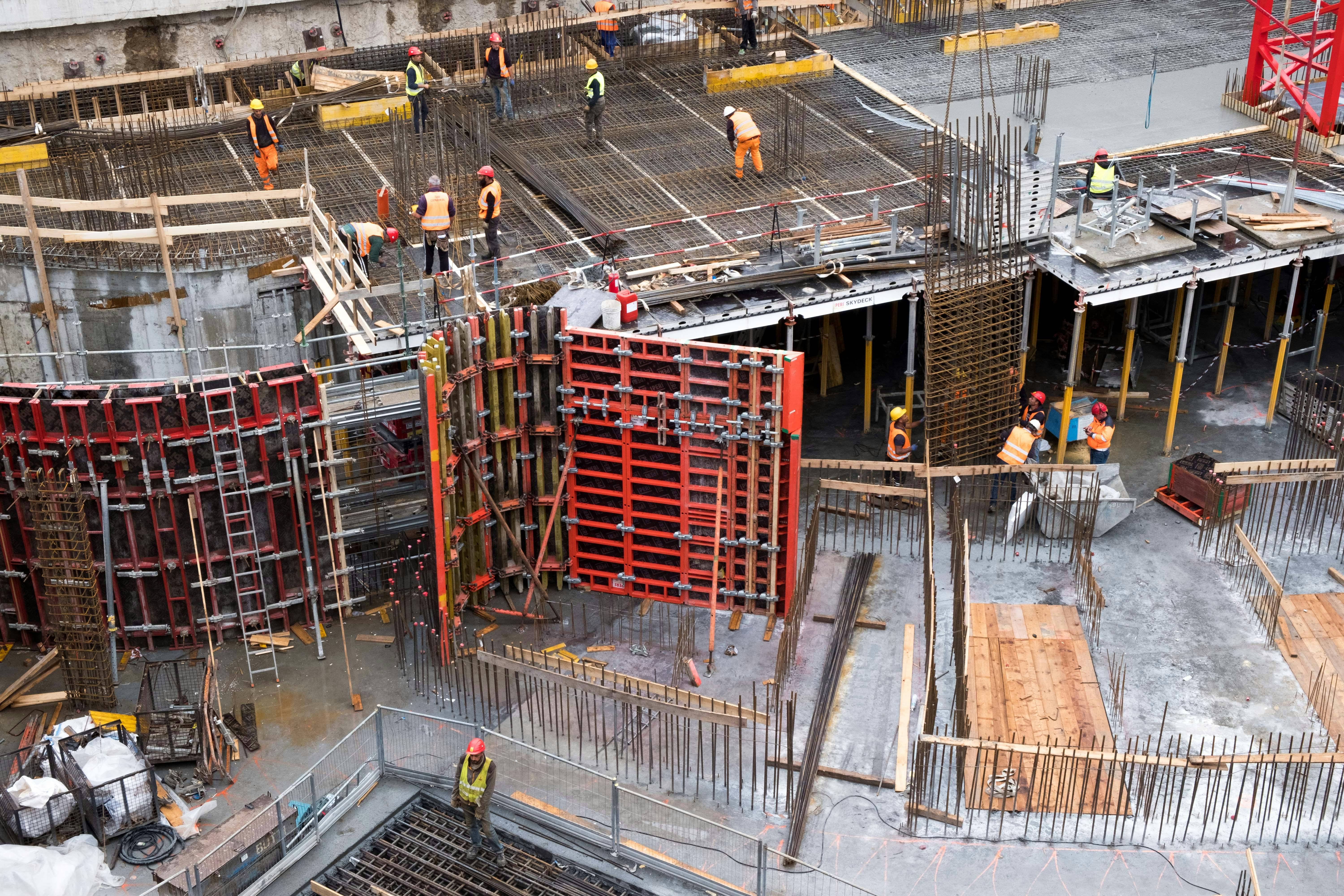 A far shot of a building under construction with men in hard hats and safety gear working at different spots