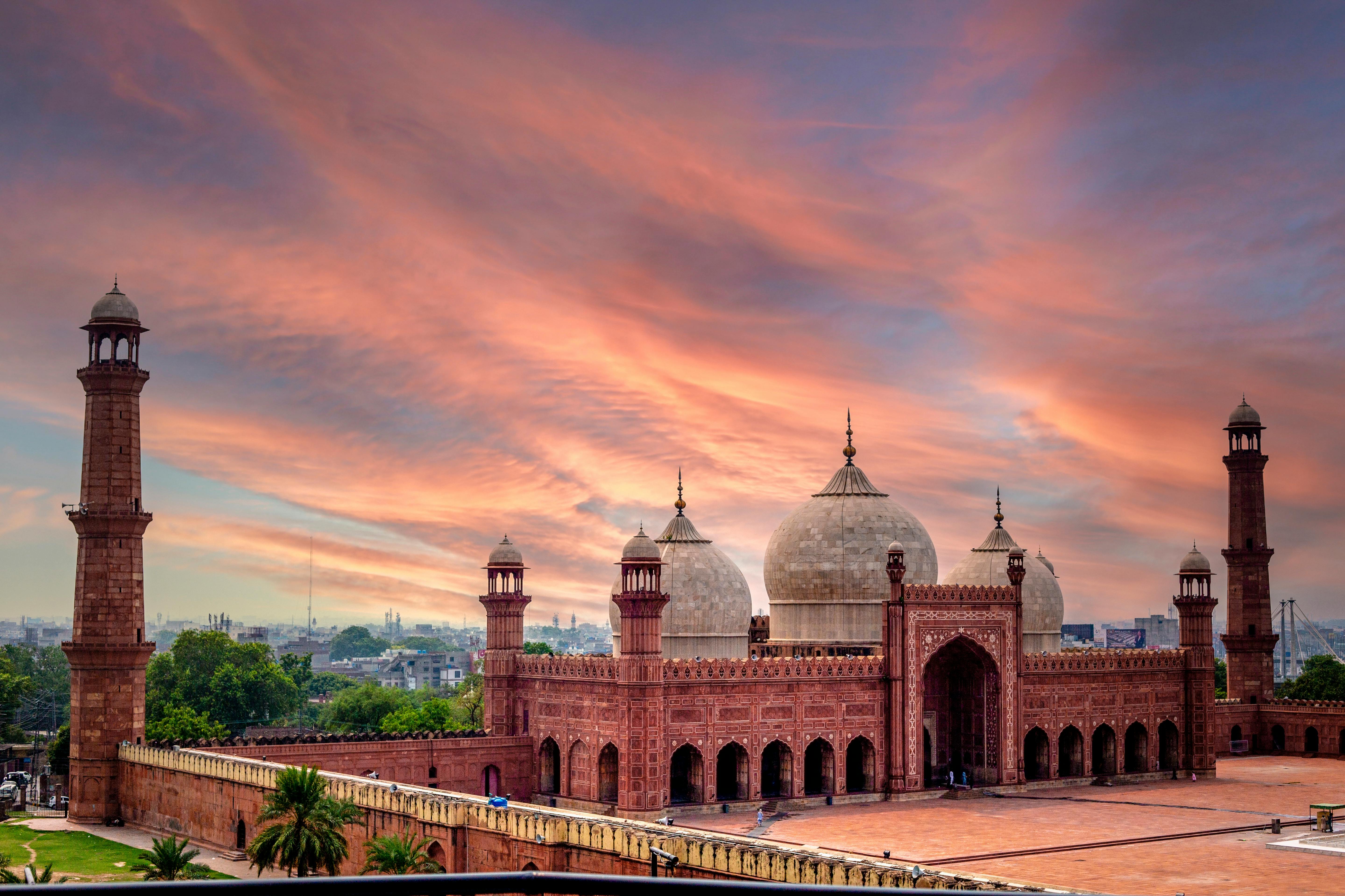 A view of the Badshahi Mosque in Lahore from a distance against a blue evening sky with salmon pink clouds