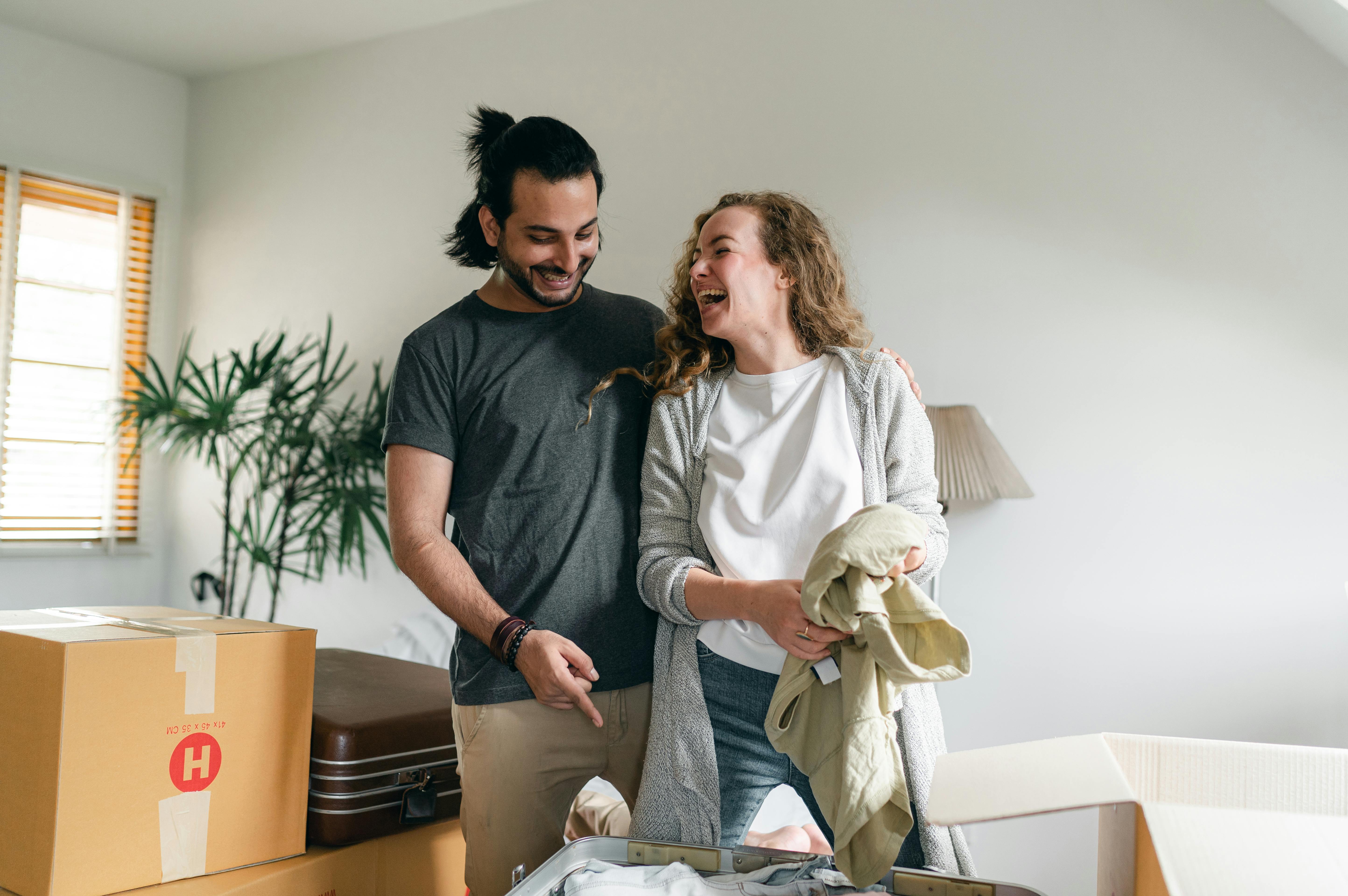 A man and woman look happy while unpacking boxes in an apartment room