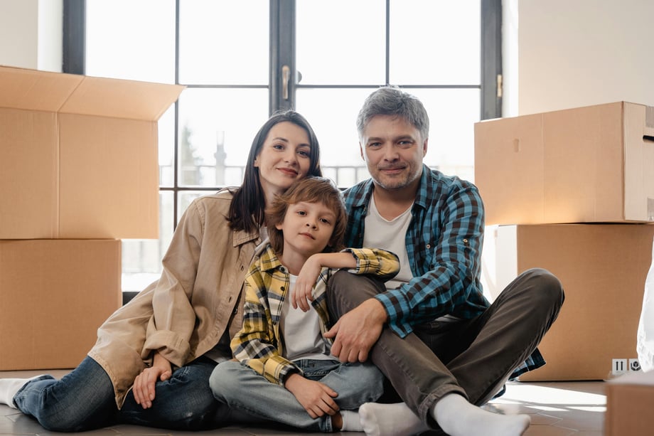 Pakistani man and woman sitting with their child among moving cartons inside a modern apartment, symbolising settling into a new home in Lahore.