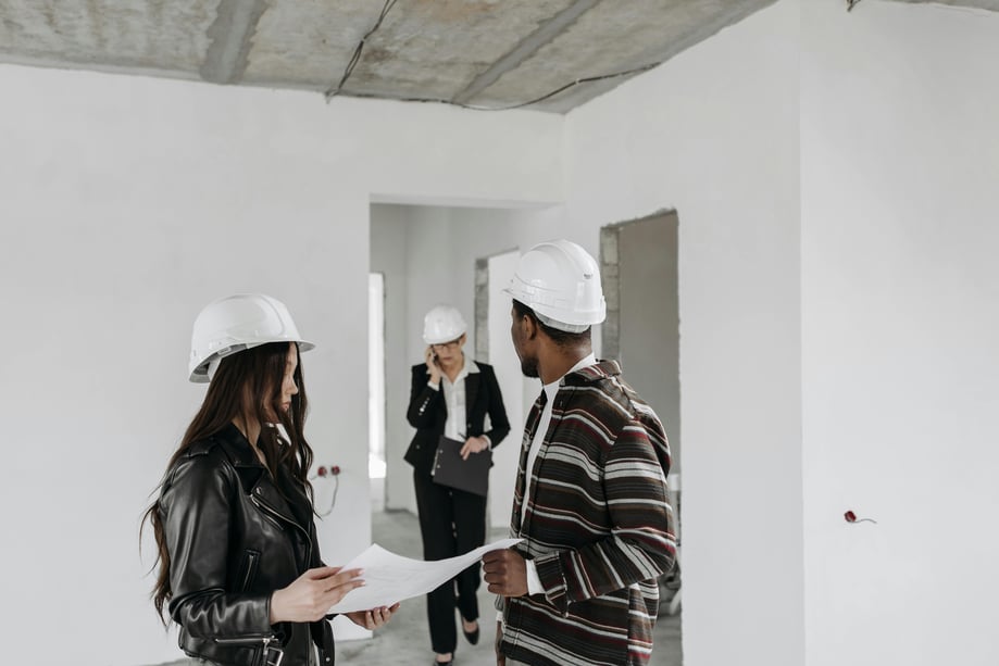 Three people in white hard hats in an unfinished room with white painted walls