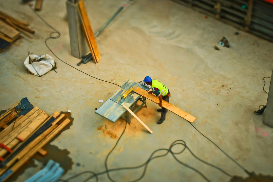 An aerial view of a person holding a plank of wood against a mechanical saw on a table at a construction site