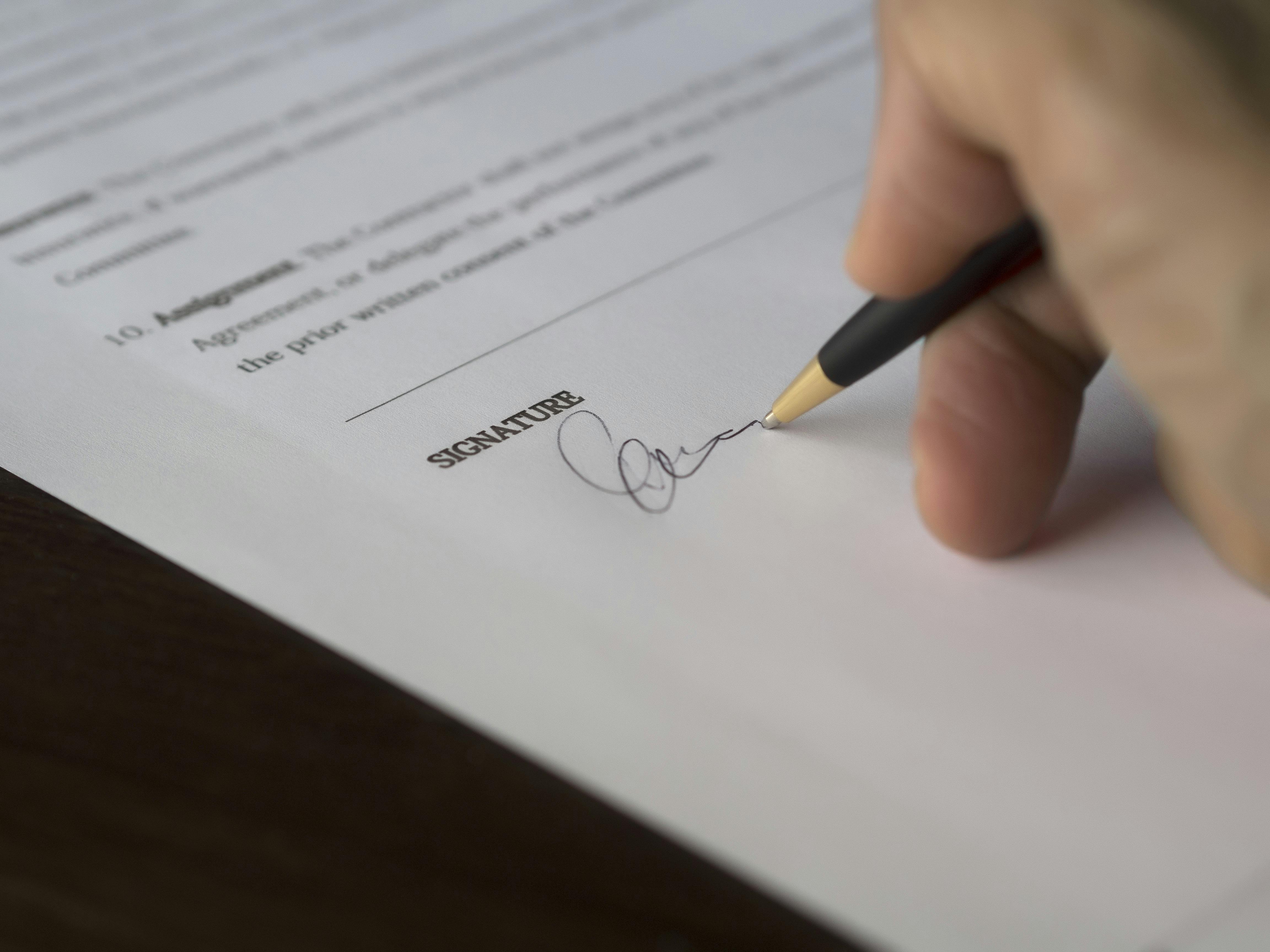 A close-up of a hand holding a black and gold pen while signing an official contract, symbolising secure and transparent property agreements aligned with British standards.