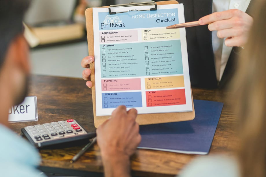 A person holds up a colourful checklist on a clipboard, showing it to two people sitting across