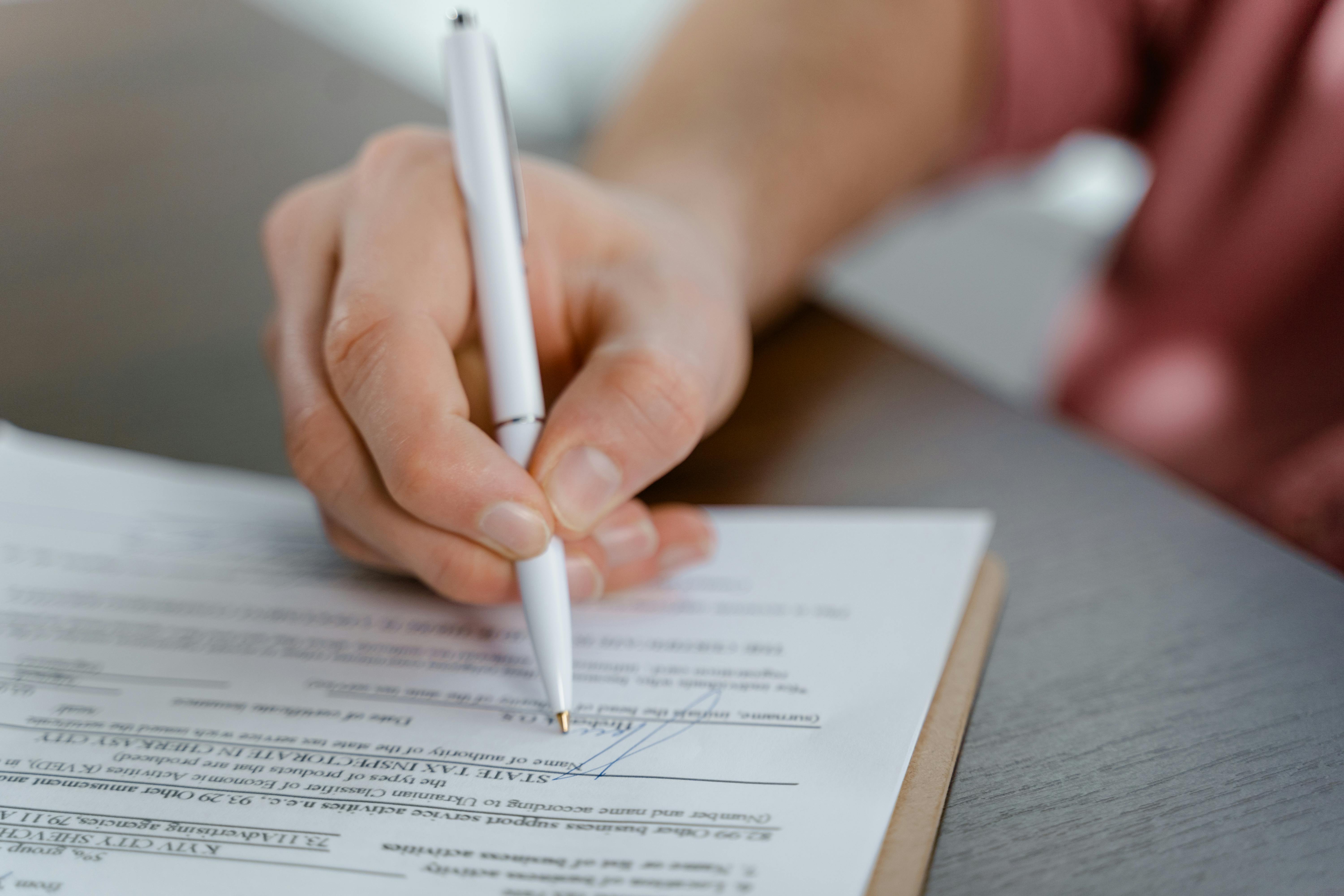 A hand holding a pen while signing a document