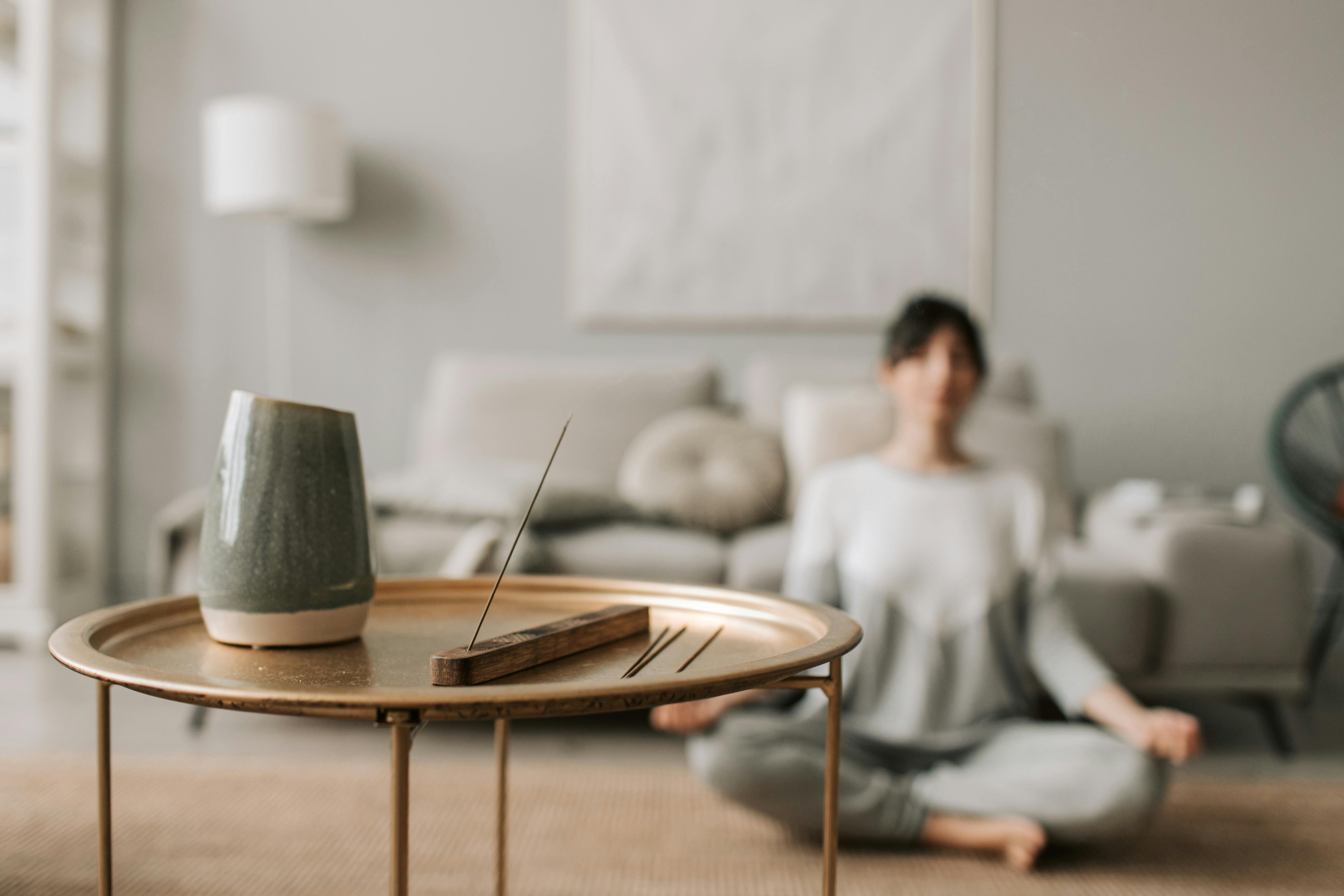 A person seated cross-legged meditating in a calm living room with a round table holding a vase and lit incense, showing the importance of wellness-led real estate in Pakistan