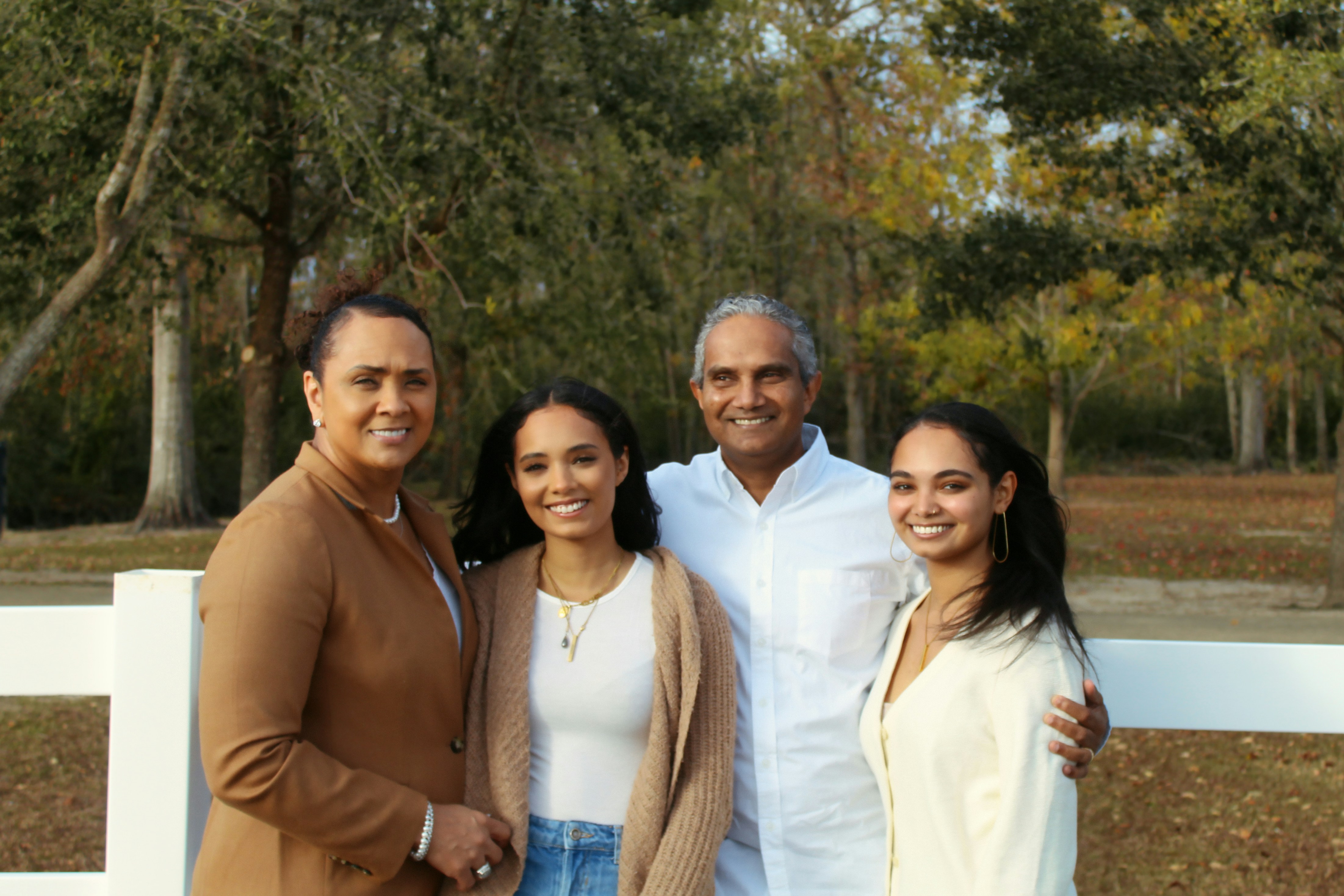 A man and woman stand with two younger girls by a fence with lush greenery in the back