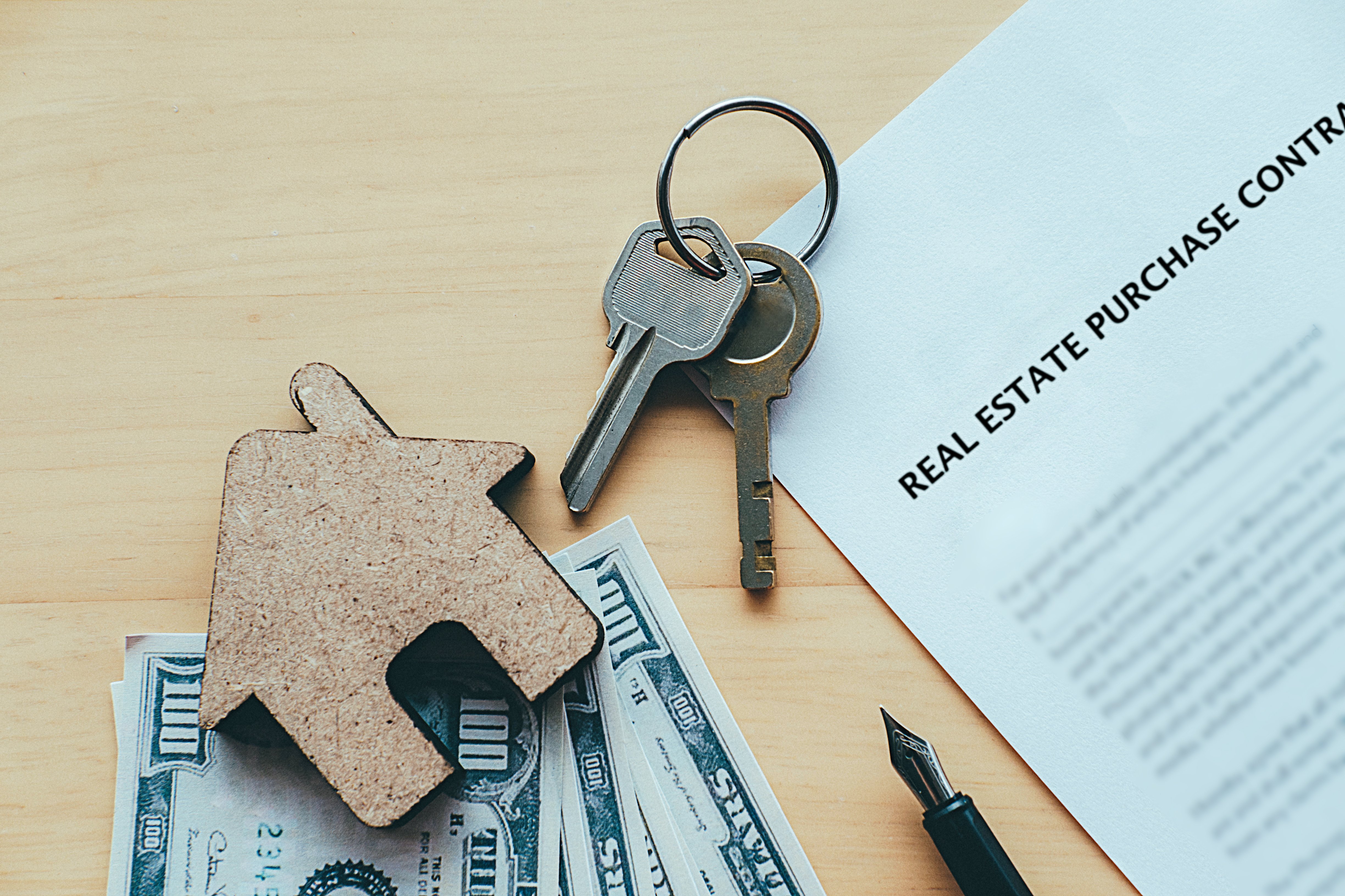 House keys, dollar bills, and a real estate purchase contract representing property investment and ROI.