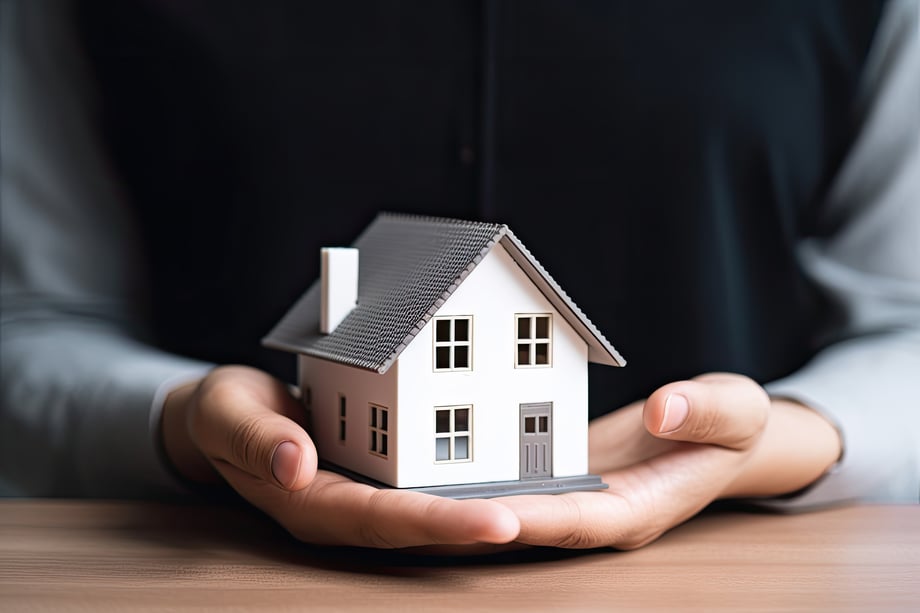 Woman presenting a miniature house symbolising the concept of home and real estate investment.